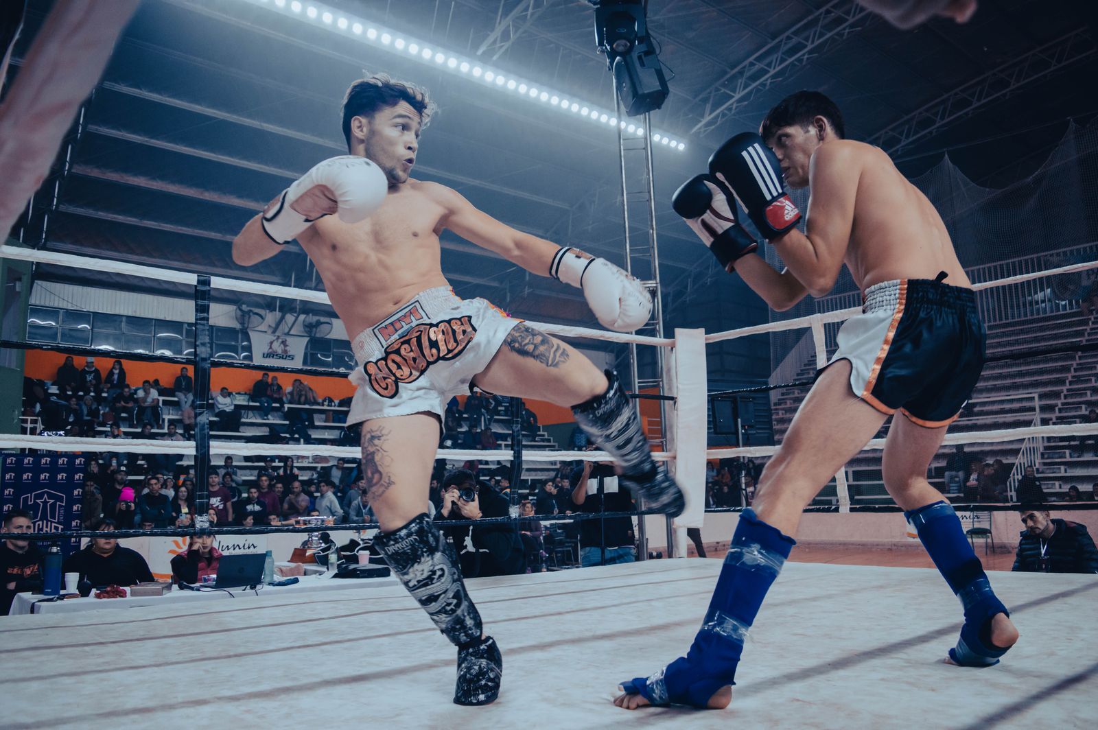 Kickboxer im Wettkampf im Ring, einer setzt einen Kick, Publikum im Hintergrund
