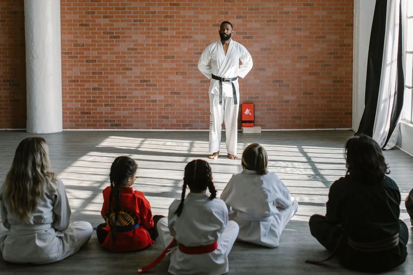 Kinder und Jugendliche sitzen im hellen Dojo vor ihrem Trainer